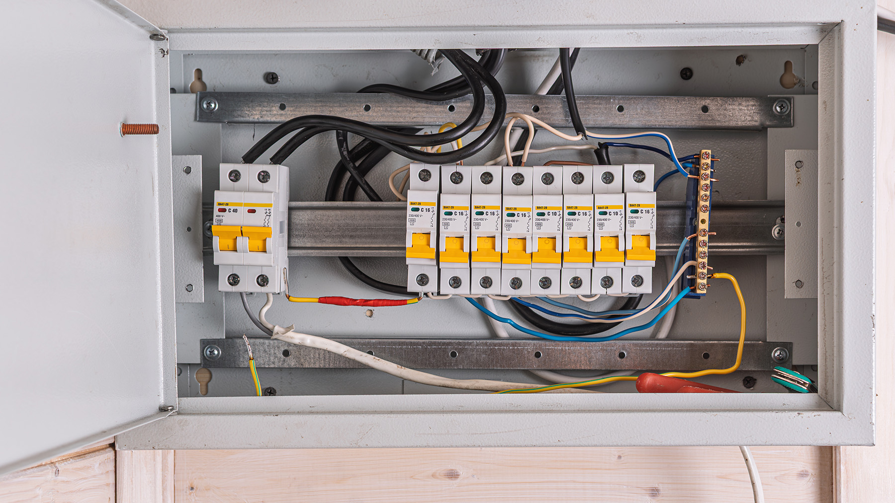 The image shows an electrical panel with various components such as switches, wires, and terminals, set against a wooden background.