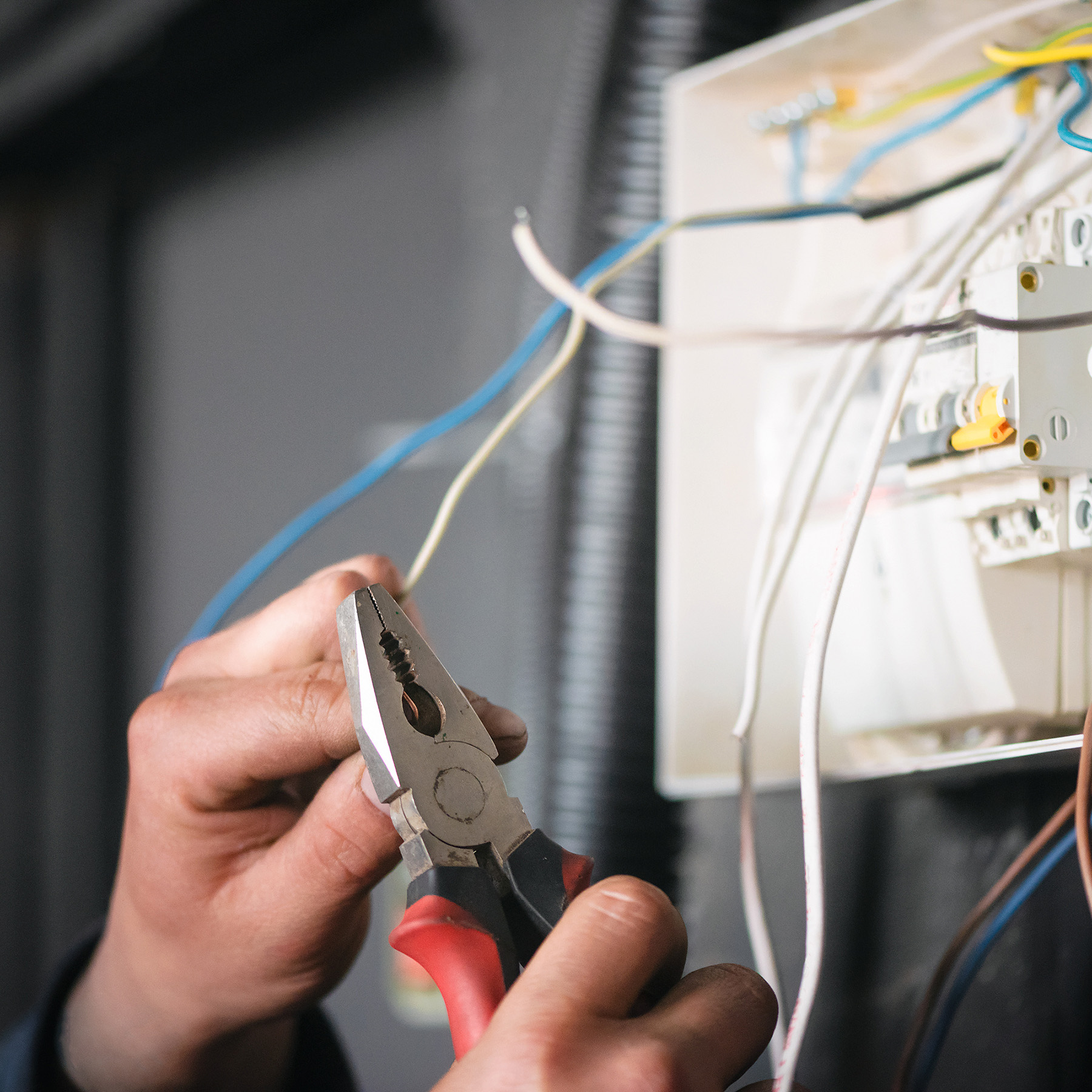 The image shows a person using a screwdriver to work on an electrical box with various wires connected to it.