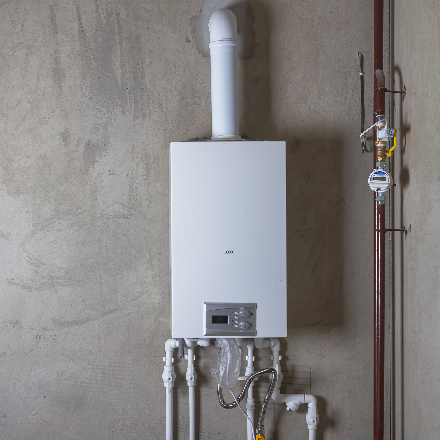 The image shows a white gas boiler with a black pipe connected to its top left corner, mounted on a wall next to a red water pipe and a yellow valve.