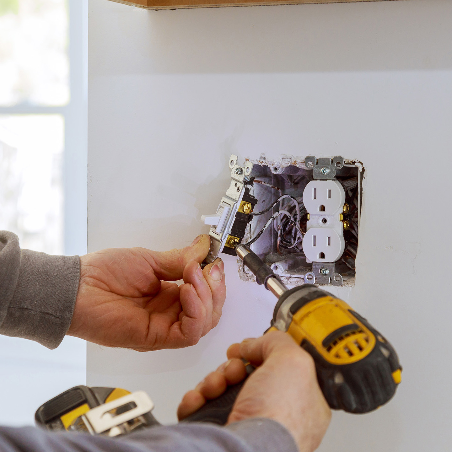 The image shows a person working on an electrical outlet, with tools and components visible, indicating a home improvement or repair activity.