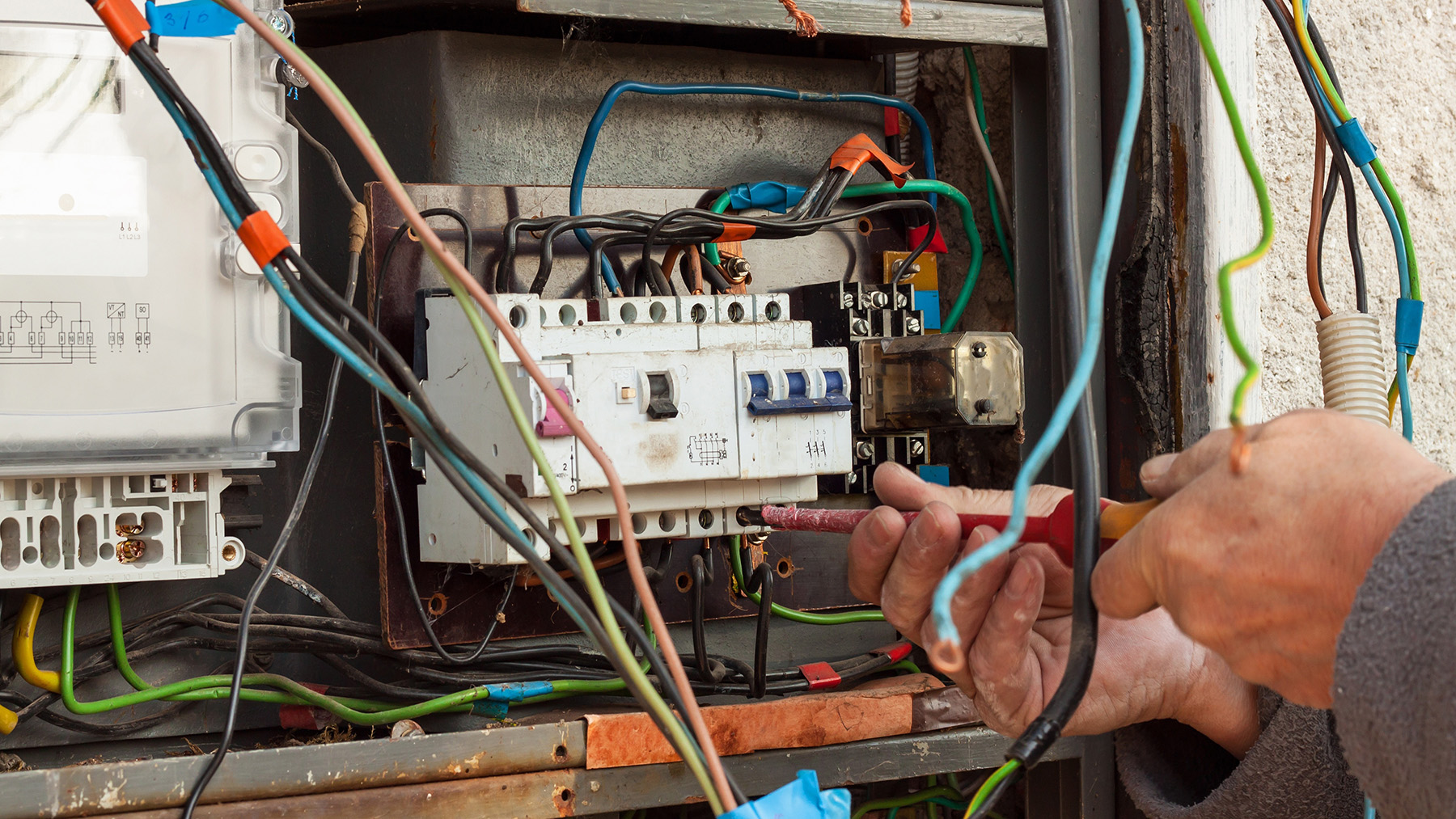 An individual working on an electrical panel with various wires and components visible.