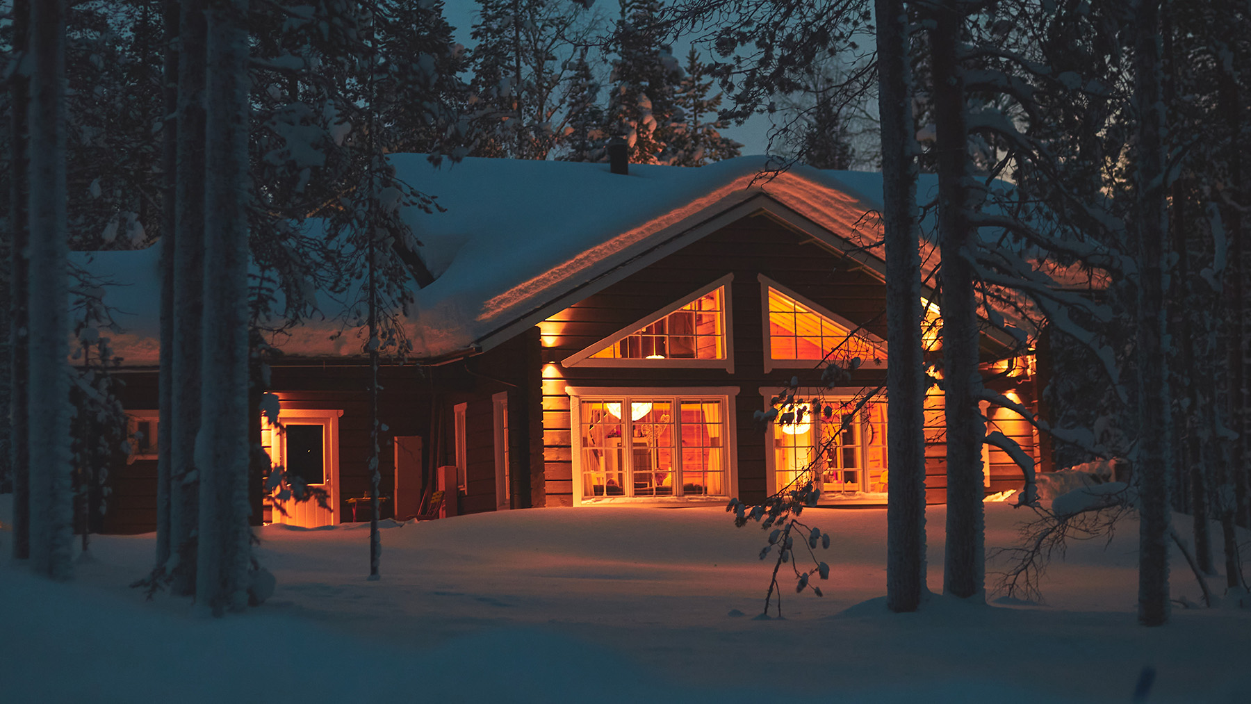 The image depicts a cozy cabin with warm lighting on a snowy night, surrounded by trees and illuminated by a soft glow from the windows.